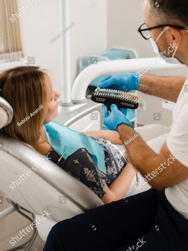 stock-photo-woman-looking-at-veneers-or-implants-teeth-color-matching-samples-in-doctor-hands-dentistry-2184452689